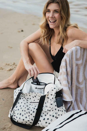 Model sitting on the beach with coco beach bag open and born in noosa heads showing inside of beach bag