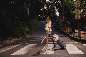 model carrying coco beach bag on suitcase across road