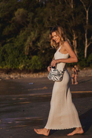 Model walking along little cove beach in white dress holding crossbody bag