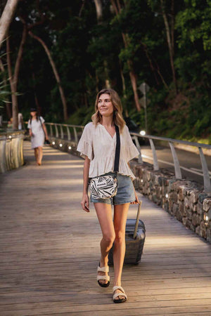 Model walking with fern gully bag and black strap and roller suitcase