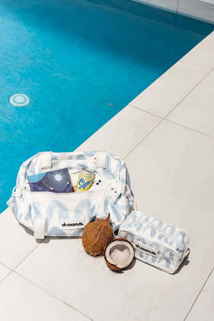 blue gym duffel bag with matching cosmetic bag sitting by a pool with a coconut