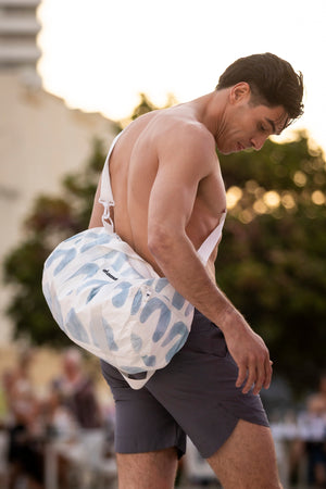 a shirtless model carrying a duffel gym bag white with blue arches crossbody