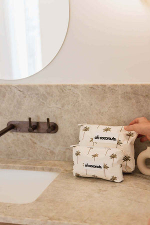 White pouch with palm tree design and 'oh coconuts' text on a bathroom counter.