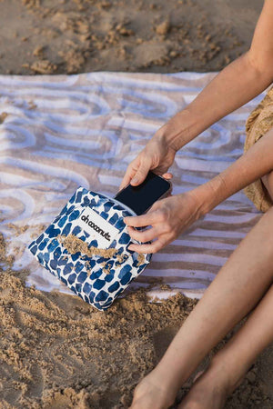 model on beach putting phone away into oh coconuts pouch. 
