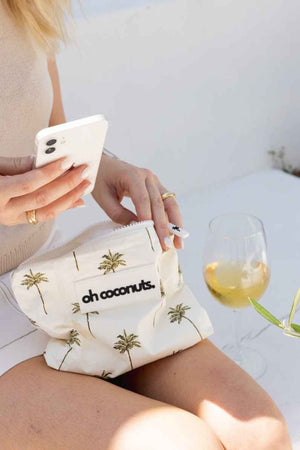 model holding palm tree pouch with phone and glass of wine