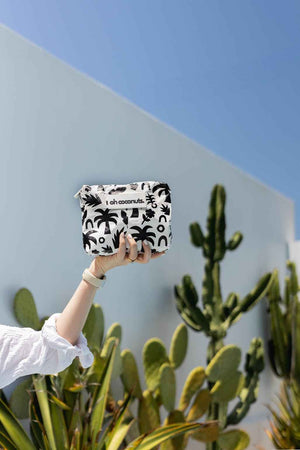 cactus background with model holding black and white palm tree pouch
