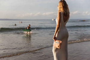model watching child in ocean while holding pink oh coconuts bag